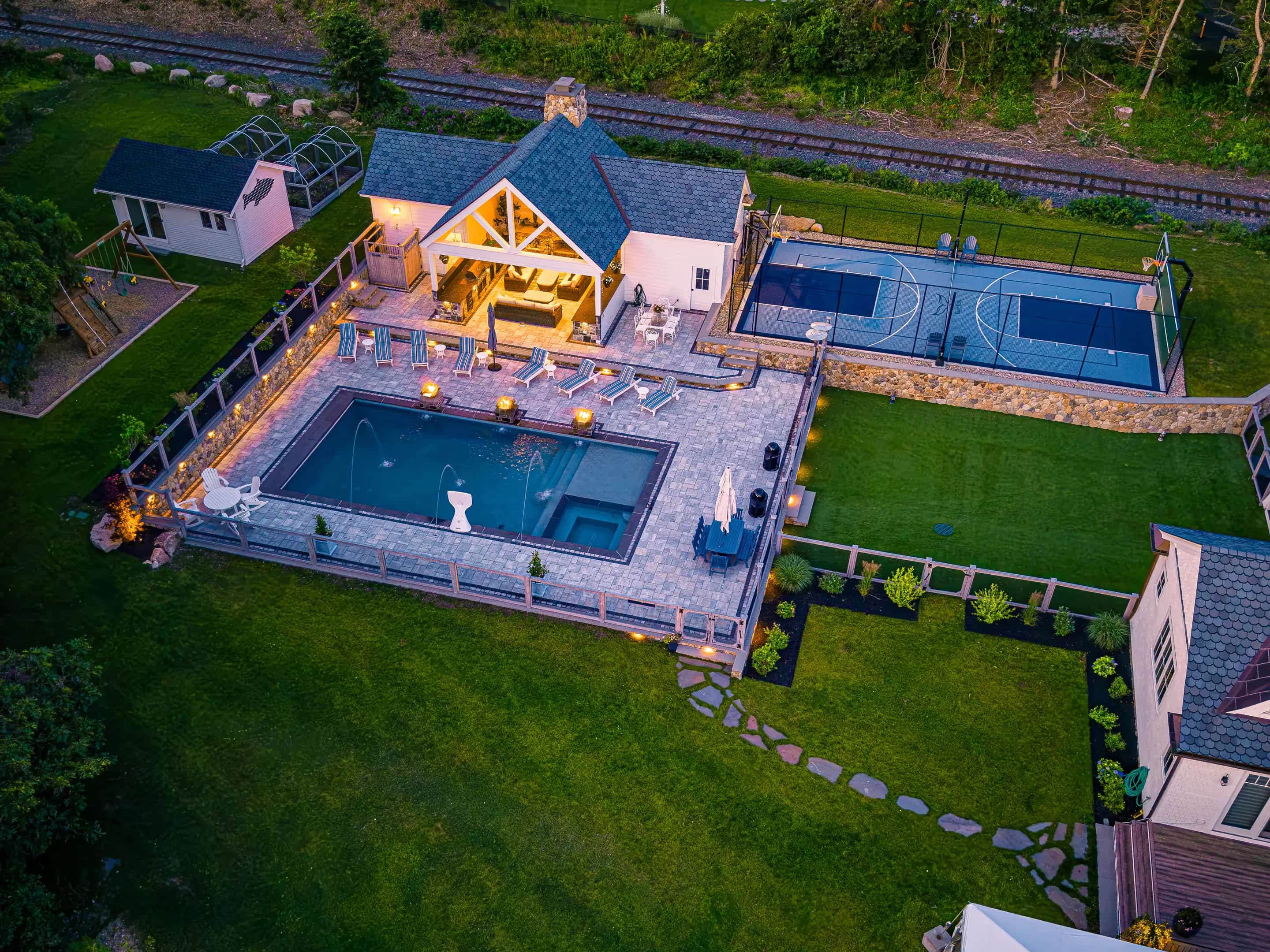 Aerial view at dusk of a lit pool deck and pavilion on a Buzzards Bay property